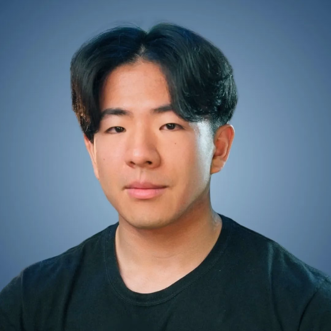 黒いTシャツを着た東アジア系の男性のポートレート。背景は青色。