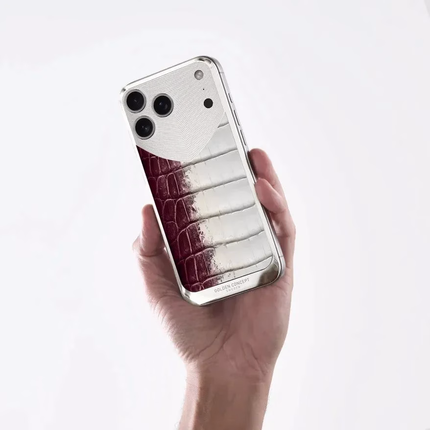 手が高級感のあるスマートフォンケースを握っている画像です。シルバーの金属部分と、赤から白へグラデーションするクロコダイル調の革素材が特徴的なツートンカラーのデザインで、底部には「GOLDEN CONCEPT」のロゴが見えます。