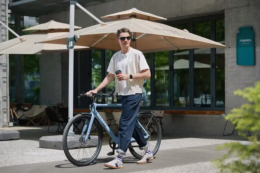 男性が電動アシスト自転車を押しながら街を歩いている様子