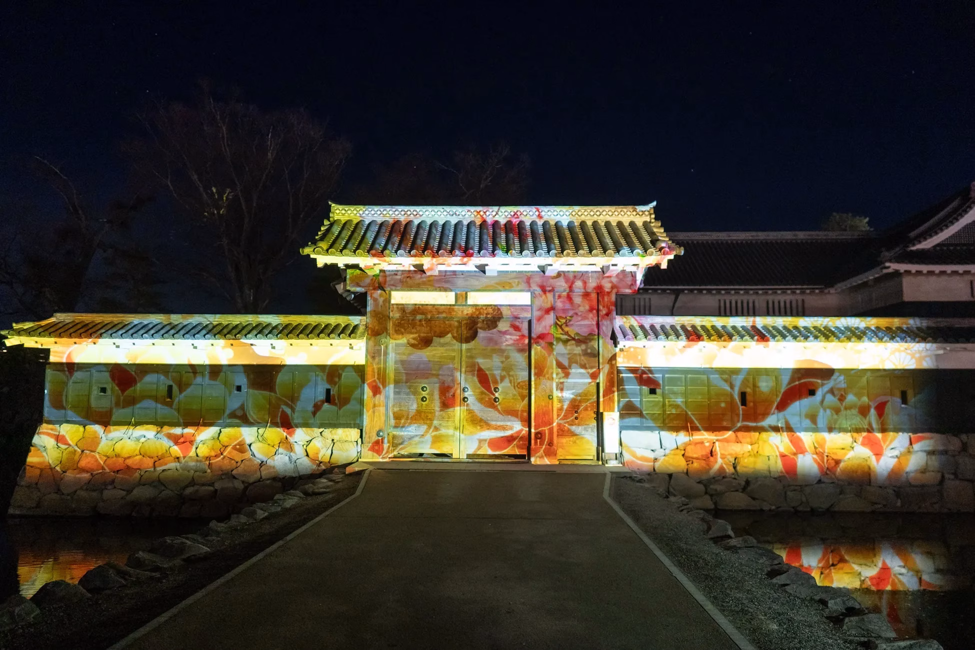 夜の城壁にプロジェクションマッピングが施された写真。鮮やかな花模様が壁や門に映し出され、幻想的な雰囲気を醸し出している。