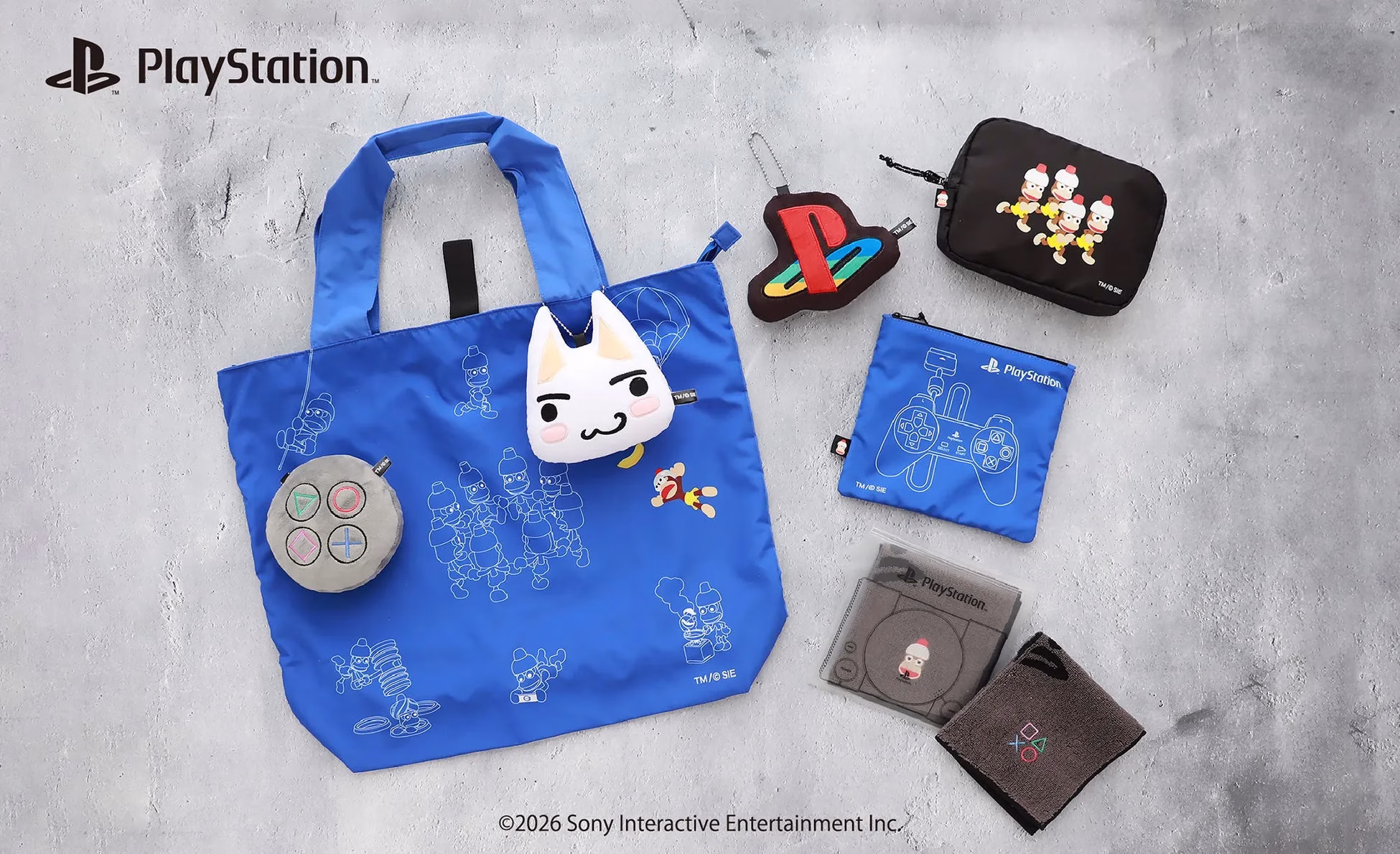 PlayStation関連のグッズが写った写真。青色のトートバッグ、ポーチ、キーホルダー、タオルなど様々なアイテムが写っている。