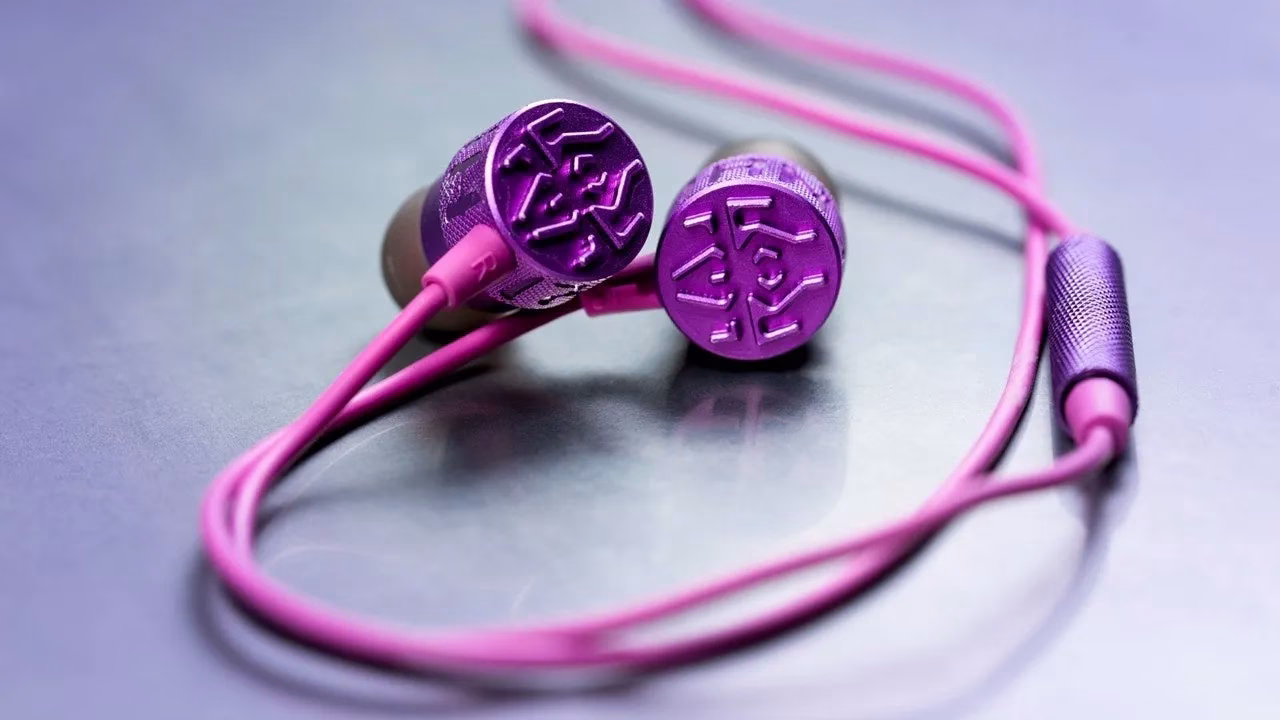 紫色のイヤホンが光沢のある表面に置かれています。イヤホンはピンク色のコードで繋がれており、鮮やかな色合いが特徴的です。