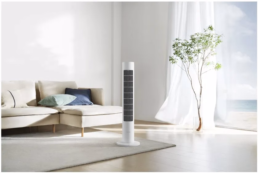 リビングルームの様子。白いタワーファンが置かれ、ソファとラグが配置されている。窓からは海が見える。