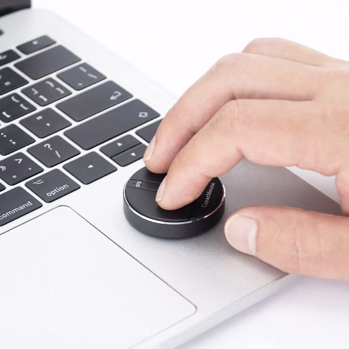 MacBookのトラックパッド上に置かれたCapaMouseを操作している手のクローズアップ画像です。CapaMouseは、黒い円形のデバイスで、人差し指で操作しています。