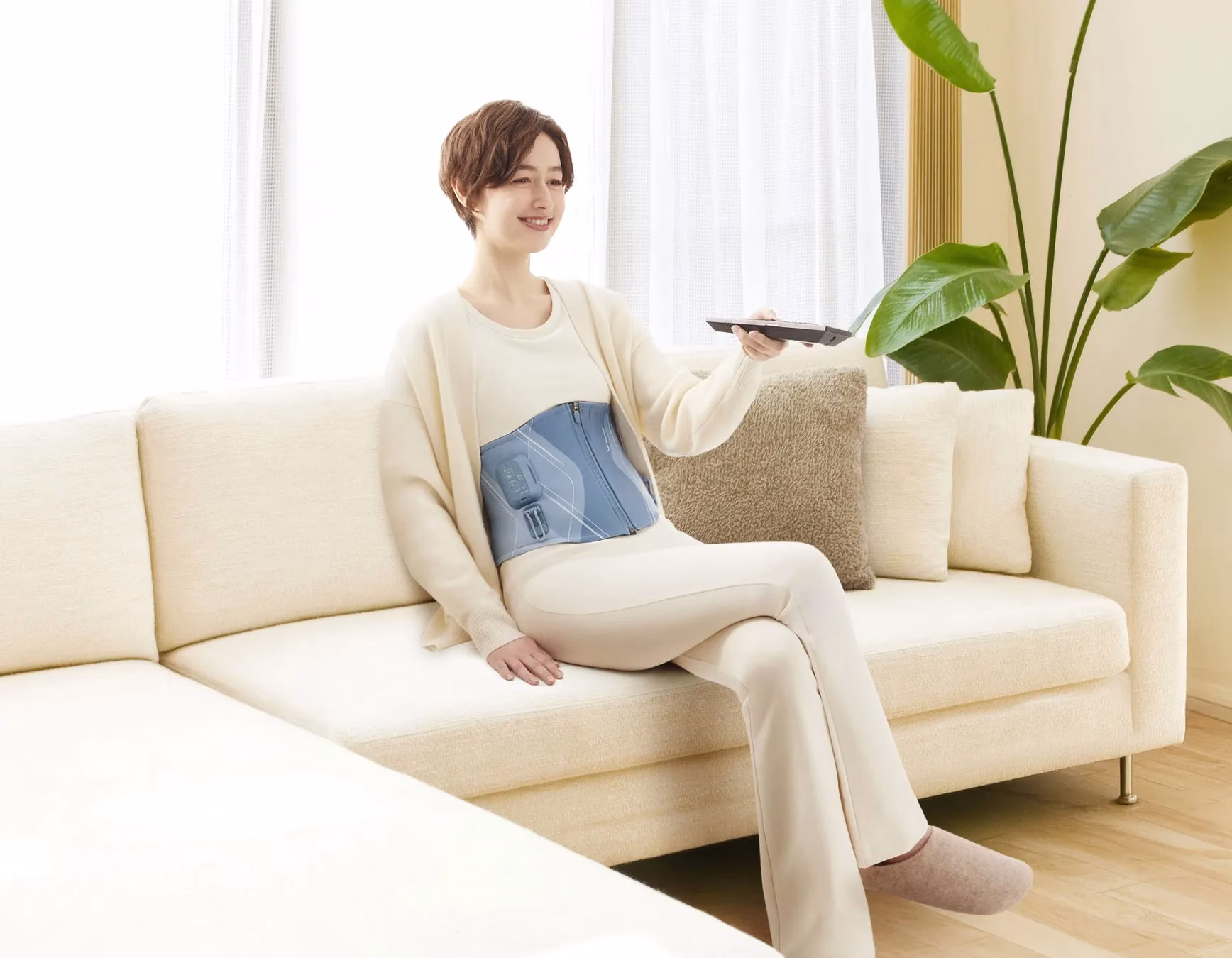女性がソファに座り、リモコンを操作している様子。腰にはサポーターを装着