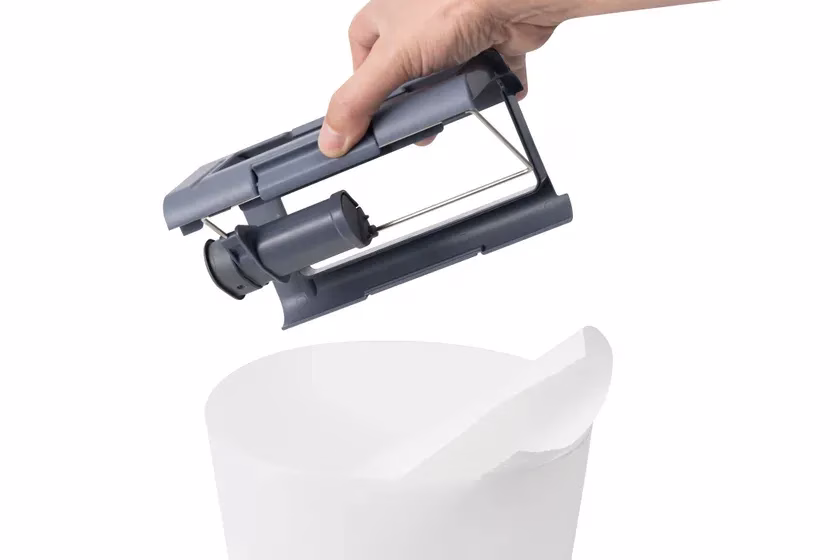 手で持たれた灰色の部品が、白い容器の上に置かれようとしている様子を描いた画像です。